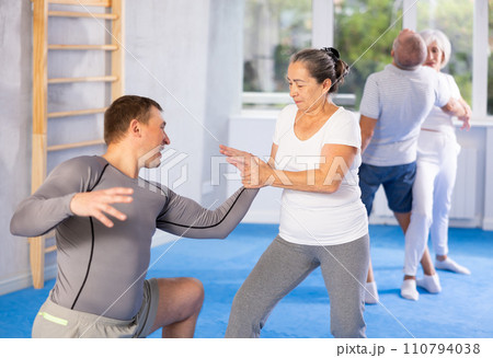 Elderly woman twists arm of attacking man with painful hold in gym. Self-defense lesson Elderly woman twists arm of attacking man with painful hold in gym. Self-defense lesson 110794038