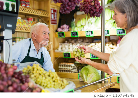 Senior salesman serving woman customer in greengrocer 110794548