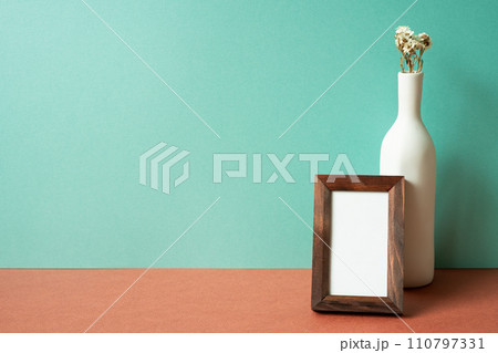 Empty wooden picture frame with white vase of dry flower on red table. mint green wall background 110797331