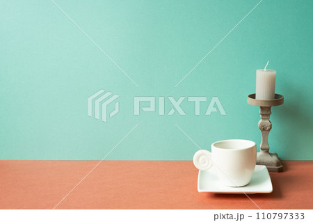 White coffee cup with candle on red table. mint green wall background White coffee cup with candle on red table. mint green wall background 110797333