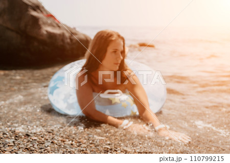 Woman summer sea. Happy woman swimming with inflatable donut on the beach in summer sunny day, surrounded by volcanic mountains. Summer vacation concept. Woman summer sea. Happy woman swimming with inflatable donut on the beach in summer sunny day, surrounded by volcanic mountains. Summer vacation concept. 110799215