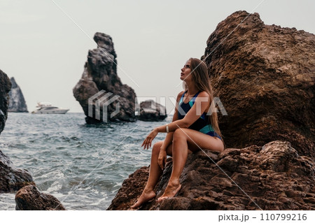 Woman summer travel sea. Happy tourist in blue bikini enjoy taking picture outdoors for memories. Woman traveler posing on the beach surrounded by volcanic mountains, sharing travel adventure journey 110799216