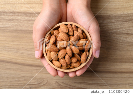 Raw almond in bowl with hand on wooden background, Table top view 110800420