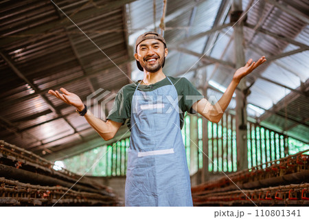 Young businessman in apron smiling at camera in chicken farm Young businessman in apron smiling at camera in chicken farm 110801341