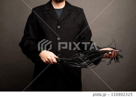male dominant holds a leather whip Flogger for hard BDSM sex with spanking 110802325