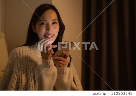 暗い部屋で深夜にスマホを見る若い女性 暗い部屋で深夜にスマホを見る若い女性 110803249