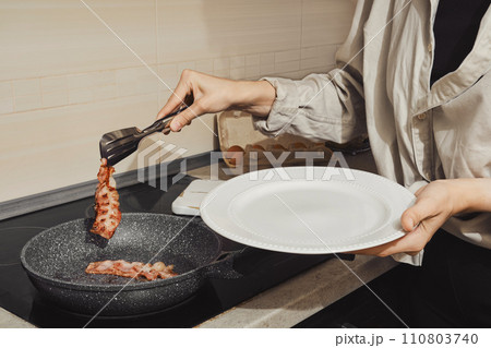 Unrecognizable woman removing fried bacon from a frying pan 110803740