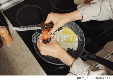 Overhead view of a woman breaking an egg into a frying pan 110803741