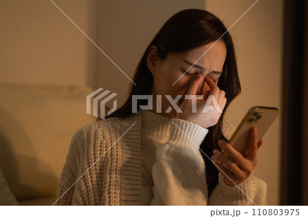 暗い部屋で夜遅くまでスマホを見て目が疲れる女性 暗い部屋で夜遅くまでスマホを見て目が疲れる女性 110803975