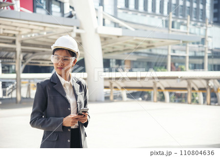 Civil women engineer wear safety white hard hat make a phone call in modern city. Young asian woman at construction site industry. Female engineer civil engineering with hard hat using smartphone. 110804636