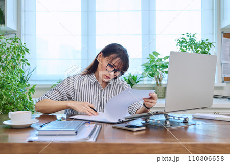 Middle-aged serious woman working at computer laptop in home office 110806658