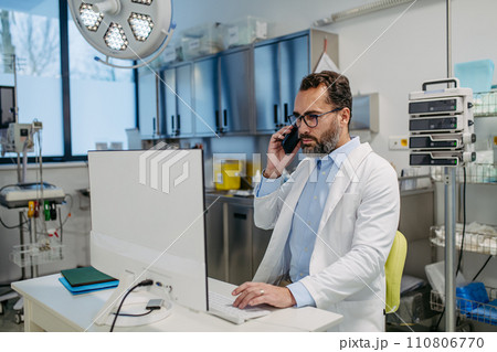 Portrait of ER doctor in hospital working in emergency room. Healthcare worker making call and typing on medical computer in emergency room. Portrait of ER doctor in hospital working in emergency room. Healthcare worker making call and typing on medical computer in emergency room. 110806770