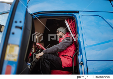 Portrait of confident professional truck driver sitting in truck cabin, looking at camera, smiling. 110806990