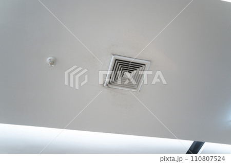 Ceiling mounted cassette type air conditioner and modern lamp light on white ceiling. Duct air conditioner for home, hall or office. Ceiling mounted cassette type air conditioner and modern lamp light on white ceiling. Duct air conditioner for home, hall or office. 110807524