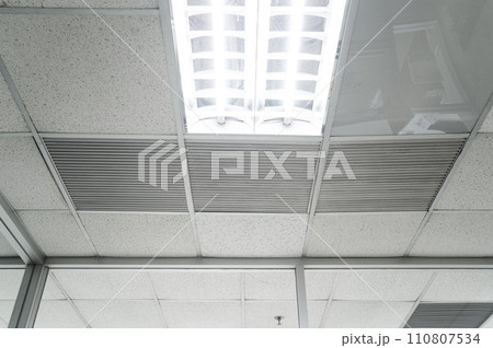Ceiling mounted cassette type air conditioner and modern lamp light on white ceiling. Duct air conditioner for home, hall or office. Ceiling mounted cassette type air conditioner and modern lamp light on white ceiling. Duct air conditioner for home, hall or office. 110807534