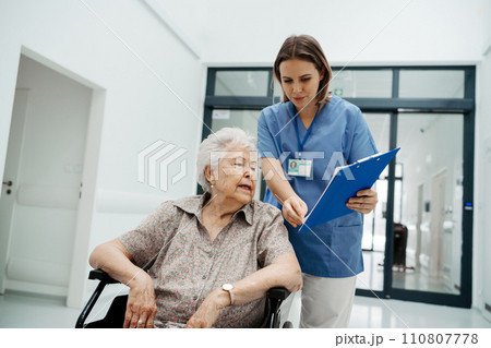 Nurse talking with senior woman, admitting a patient to the hospital, filling documents. Discharging of elderly patient. after surgery. Nurse talking with senior woman, admitting a patient to the hospital, filling documents. Discharging of elderly patient. after surgery. 110807778