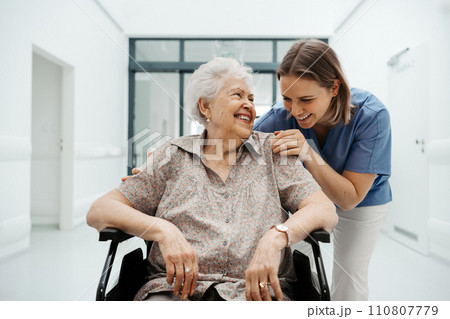 Portrait of nurse and senior patient talking in hospital corridor. Emotional support for elderly woman. 110807779