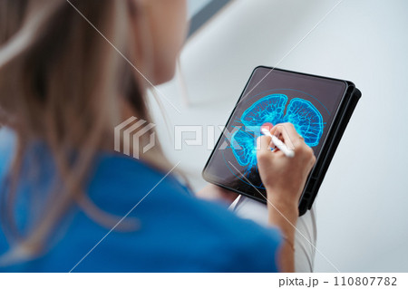 Portrait of female doctor sitting in office, looking at test results CT scans in tablet. Female surgeon in modern medical clinic. 110807782