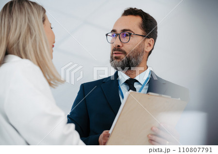 Pharmaceutical sales representative talking with female doctor in medical building. Hospital director consulting with healthcare staff. 110807791
