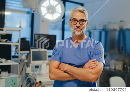Portrait of confident ER doctor standing in hospital emergency room. Handsome doctor in scrubs holding clipboard, standing in modern private clinic. 110807793