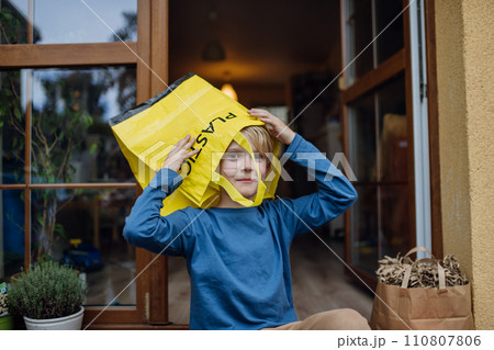 Boy put recycling bag for plastic waste on head. Boy sorting the waste according to material into colored bags. 110807806