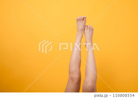 Indulge in the velvety touch of elegance with a 30s person's close up legs against a vibrant yellow backdrop. Gentle and smooth foot concept. 110808554