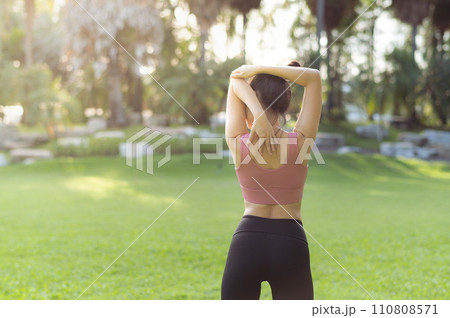 Female jogger. Fit young 30s Asian woman with pink sportswear stretching muscle in park before running and enjoying a healthy outdoor. Fitness runner girl in public park. Wellness being concept 110808571