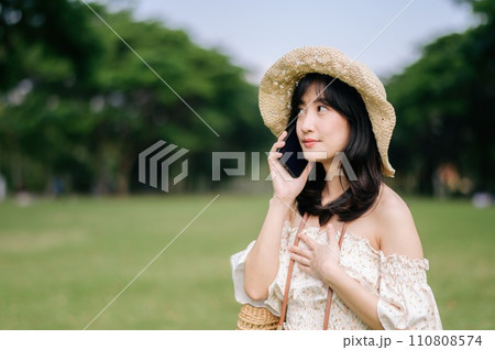 Portrait of asian young woman traveler with weaving hat, basket, mobile phone and camera on green public park background. Journey trip lifestyle, world travel explorer or Asia summer tourism concept. 110808574