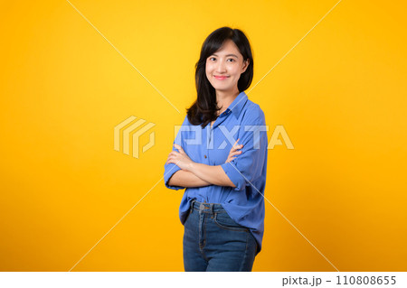 Radiate confidence with captivating portrait. A young Asian woman wearing a blue shirt showcases happy smile while crossing her arms. Perfect for conveying a sense of self-assurance and determination. 110808655