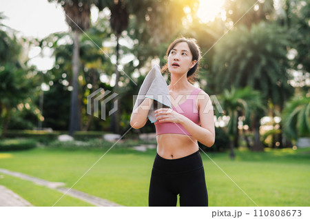 beauty of a healthy lifestyle as a 30s Asian woman in pink sportswear wipes her cheek after a sunset run in the public park. Achieve fitness goals and embrace accomplishment beauty of a healthy lifestyle as a 30s Asian woman in pink sportswear wipes her cheek after a sunset run in the public park. Achieve fitness goals and embrace accomplishment 110808673