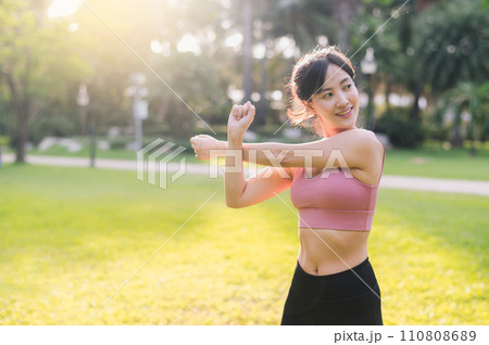 wellness and healthy lifestyle portrait of 30s Asian woman in pink sportswear. preparing and stretching body and arm muscles before sunset run in the park. fitness outside and embrace balanced life. 110808689