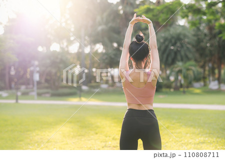 wellness and healthy lifestyle portrait 30s Asian woman in pink sportswear. preparing and stretching arm muscles before sunset run in the park. fitness outside and balanced life concept. 110808711