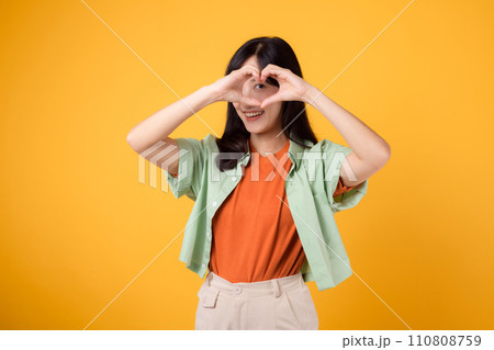 healthcare and wellness guided by an Asian woman in her 30s. Let her heart hand gesture on a vibrant yellow background inspire your journey towards body wellness 110808759
