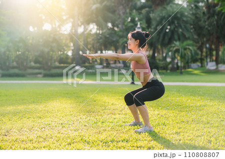 Healthy outdoor lifestyle with fit young Asian woman 30s wearing pink sportswear squat muscles in public park before going for invigorating run, embodying the wellness concept. 110808807