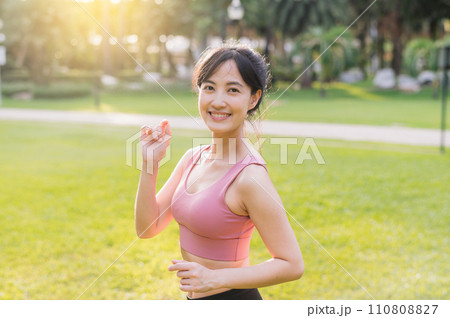 Capture the essence of wellness living as a happy, beautiful 30s Asian woman smiles and looks at the camera in a park at sunset. Capture the essence of wellness living as a happy, beautiful 30s Asian woman smiles and looks at the camera in a park at sunset. 110808827