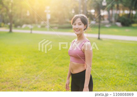 Experience the joy of a happy, fit female jogger in her 30s. Asian woman wearing pink sportswear, enjoying fresh air in a public park. Embrace wellness living and connect with nature. 110808869