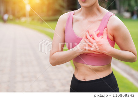 Woman jogger. young asian female wearing pink sportswear holding hands on chest after running in public park. Healthcare exercise pain concept. 110809242
