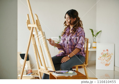 Smiling girl enjoying painting picture on easel in art class Smiling girl enjoying painting picture on easel in art class 110810455