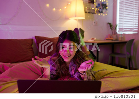 Excited girl lying on bed when video calling her best friend at night Excited girl lying on bed when video calling her best friend at night 110810501
