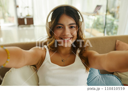 Happy teenage girl in headphones video calling her friend or family members 110810559
