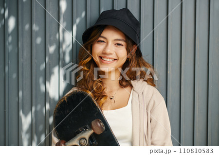 Portrait of happy girl in bucket hat holding skateboard Portrait of happy girl in bucket hat holding skateboard 110810583