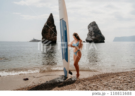 Woman sea sup. Close up portrait of happy young caucasian woman with long hair looking at camera and smiling. Cute woman portrait in bikini posing on sup board in the sea Woman sea sup. Close up portrait of happy young caucasian woman with long hair looking at camera and smiling. Cute woman portrait in bikini posing on sup board in the sea 110811688