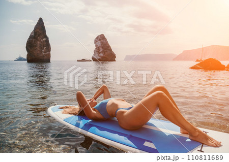 Woman sea sup. Close up portrait of happy young caucasian woman with long hair looking at camera and smiling. Cute woman portrait in bikini posing on sup board in the sea Woman sea sup. Close up portrait of happy young caucasian woman with long hair looking at camera and smiling. Cute woman portrait in bikini posing on sup board in the sea 110811689