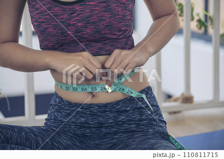 Sport Women home fitness measure waist after workout exercise in living room. Close up Young woman hands using measurement tape in sportswear. Body weight traning healthy lifestyle diet concept 110811715