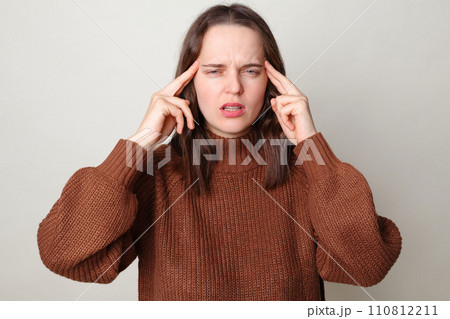 Tired sick unhealthy brown haired adult woman wearing brown sweater posing isolated over gray background suffering from headache feeling pain having migraine symptoms being overworked Tired sick unhealthy brown haired adult woman wearing brown sweater posing isolated over gray background suffering from headache feeling pain having migraine symptoms being overworked 110812211