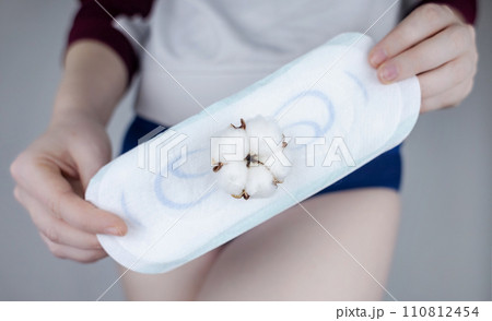Sanitary napkin and cotton plant flower. The girl shows a cotton sanitary pad against the background of her panties. Concept of plastic-free products for women menstruation. Eco friendly products Sanitary napkin and cotton plant flower. The girl shows a cotton sanitary pad against the background of her panties. Concept of plastic-free products for women menstruation. Eco friendly products 110812454