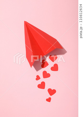 Red paper airplane with hearts on a pink background. 110812634