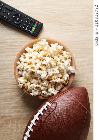 A bowl with popcorn, a rugby ball and a remote control A bowl with popcorn, a rugby ball and a remote control 110812722