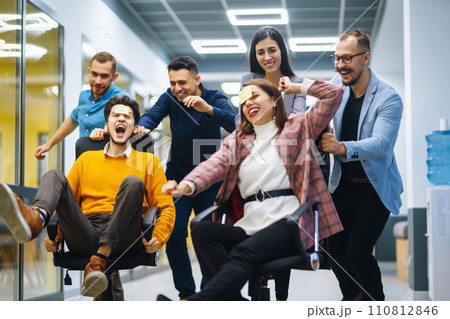 Young cheerful business people racing on office chairs and laughing. Funny activity Young cheerful business people racing on office chairs and laughing. Funny activity 110812846