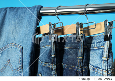 Ukraine, Kyiv, 28.10.2023 Jeans hang on hangers on a blue background Ukraine, Kyiv, 28.10.2023 Jeans hang on hangers on a blue background 110812993